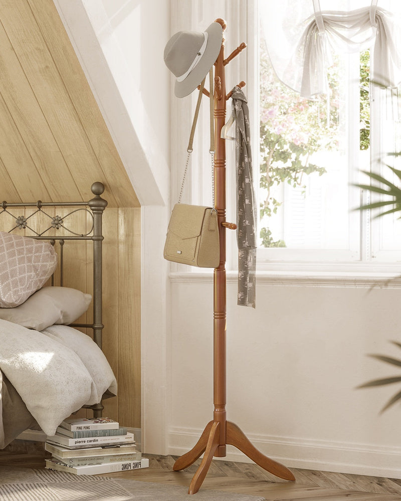 Caramel brown coat rack stand in a bedroom beside a bed holding a hat, bag and scarf