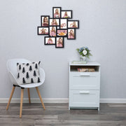 Black collage frame hung on a grey wall above a white bedside unit and chair