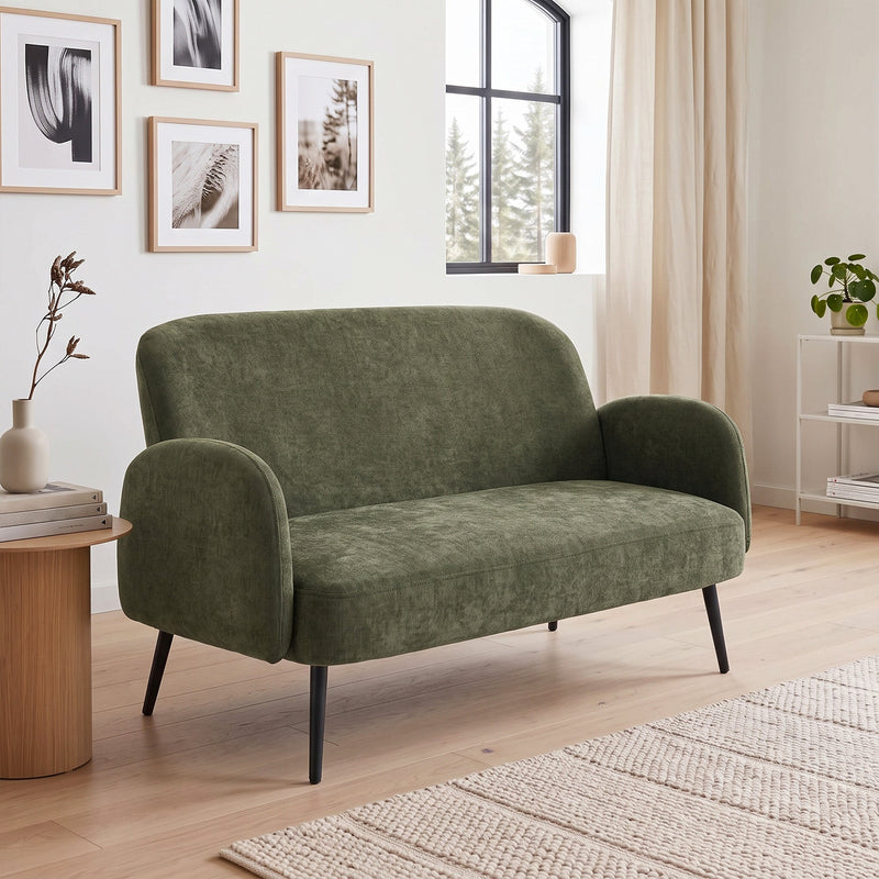 Green 2 seater sofa in a living room with framed prints and a woven rug