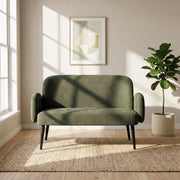 Green sofa in a bright room beside a window, a plant and a framed print