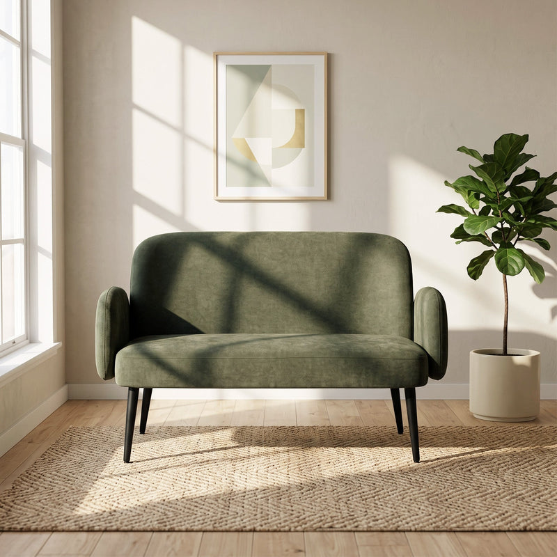 Green sofa in a bright room beside a window, a plant and a framed print
