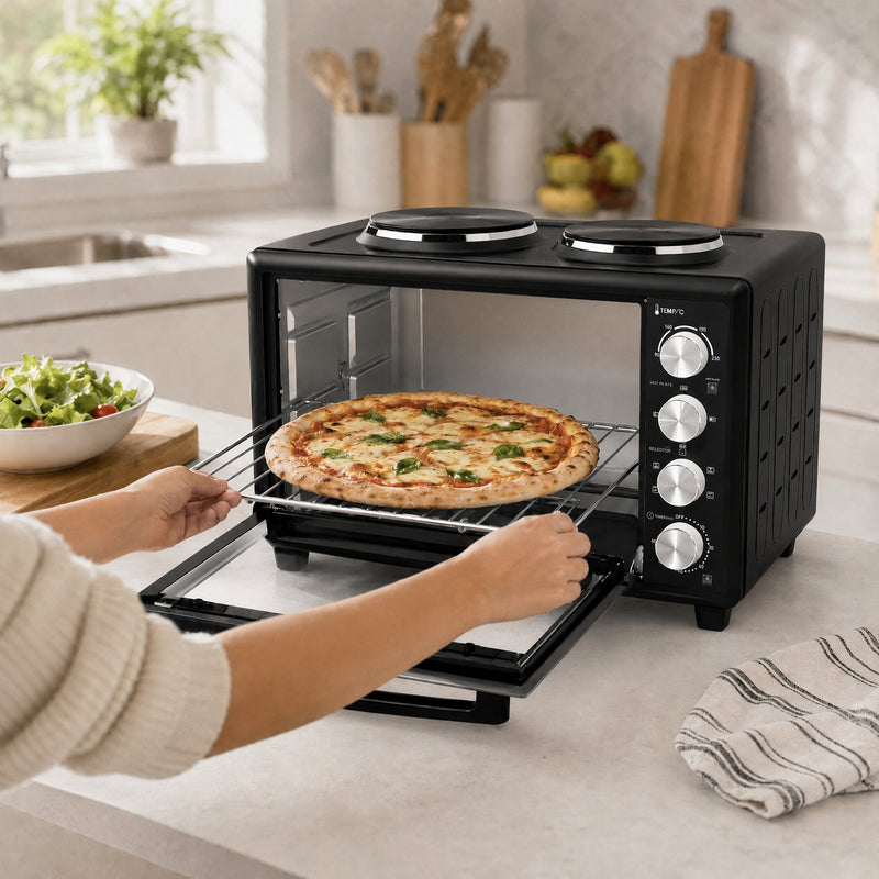 Hands lifting a cooked margherita pizza on the wire rack out of the open mini oven door
