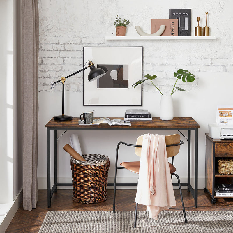 Computer desk against a white brick wall with a lamp, books and a chair