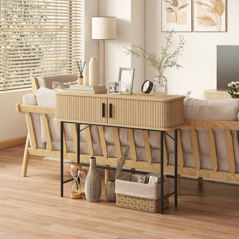 Console table behind a sofa holding a lamp, books, photo frames and a basket underneath