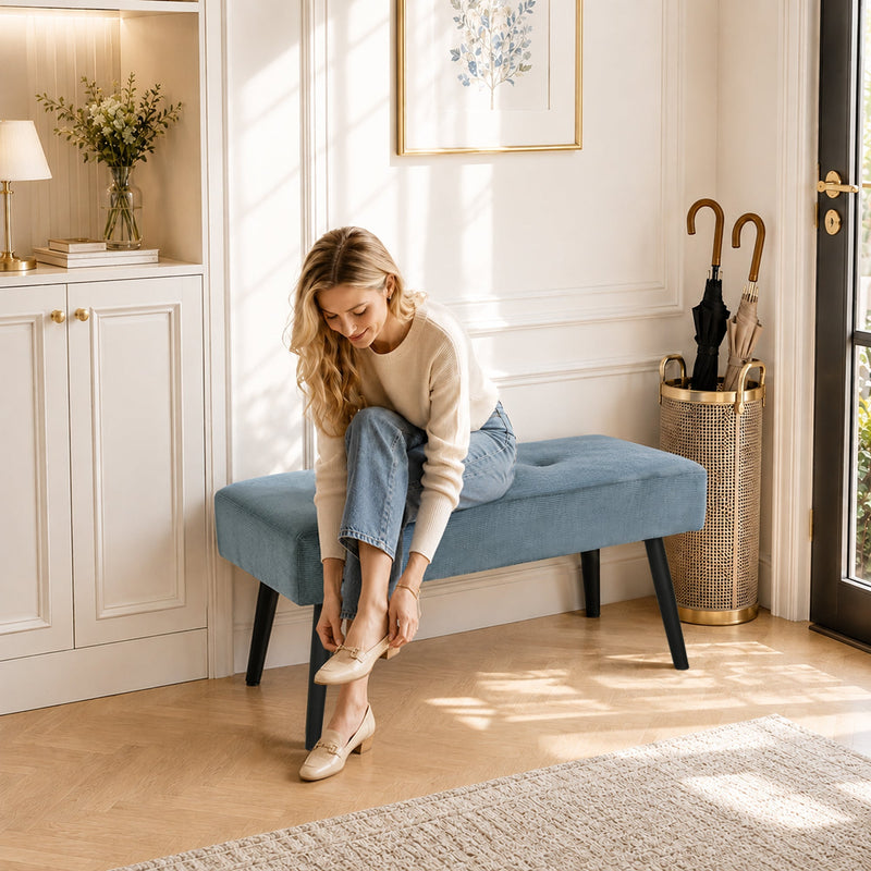 Woman sitting on the blue entryway bench putting on shoes by the front door