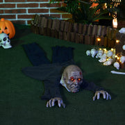Crawling zombie prop lying on grass at night beside a pumpkin and small skulls