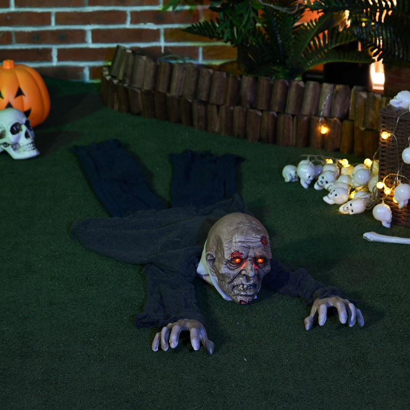 Crawling zombie prop lying on grass at night beside a pumpkin and small skulls