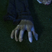 Close-up of the crawling zombie prop's pale outstretched hand resting on grass