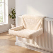 Cream cat bed hanging on a white radiator in a bright room