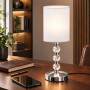 Bedside lamp switched on beside a leather notebook and smartphone on a desk