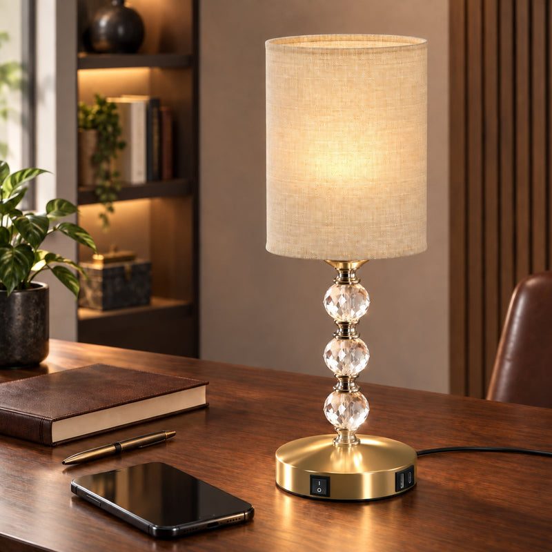 Crystal table lamp lit on a wooden desk beside a notebook and phone
