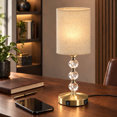 Crystal table lamp lit on a wooden desk beside a notebook and phone
