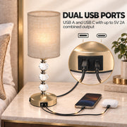 Dual USB ports graphic with a phone and earbuds charging from the lamp base on a bedside table