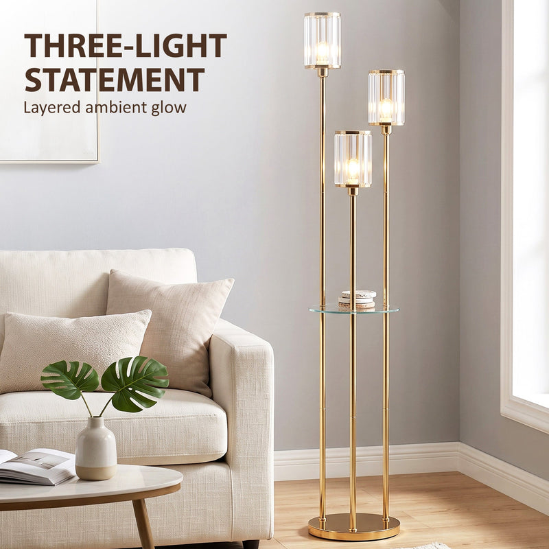 Three-light gold tone floor lamp styled in a living room with a sofa and plant