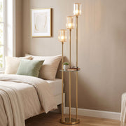 Gold tone 3-light floor lamp and glass shelf next to a bed and bedside art