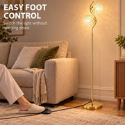 Foot pressing the floor-level cord switch of a gold crystal globe floor lamp beside a sofa