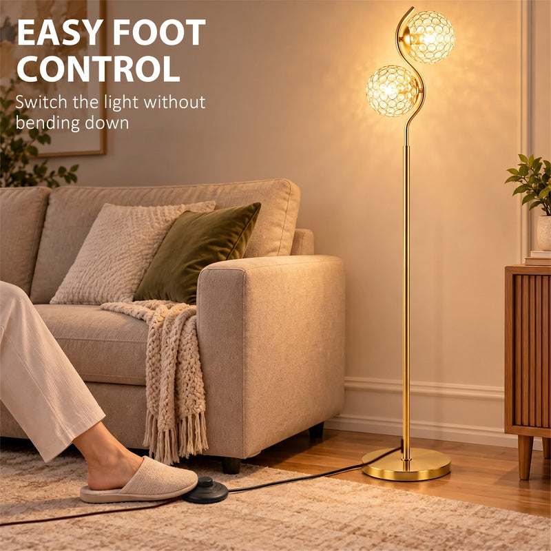 Foot pressing the floor-level cord switch of a gold crystal globe floor lamp beside a sofa
