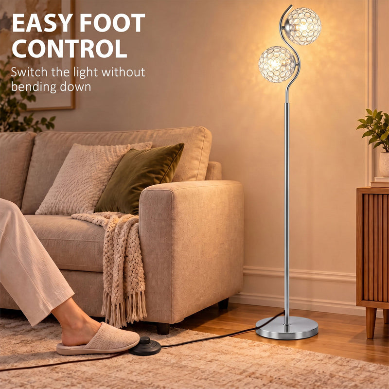 Foot pressing the floor-level cord switch of a silver crystal globe floor lamp beside a sofa