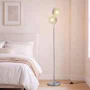 Silver crystal globe floor lamp lit beside a white bed in a bright bedroom