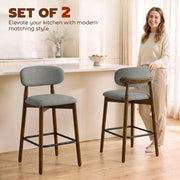 Woman standing in a kitchen beside two grey curved-back bar stools