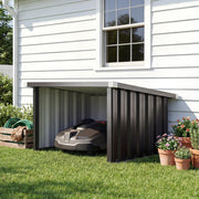 Robot mower garage beside a white house wall sheltering a robotic mower
