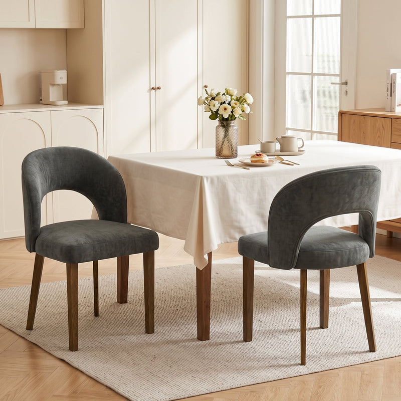 Two dark grey chenille chairs beside a cream-clothed dining table in a kitchen