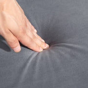 Close-up of a hand pressing into the tufted velvet seat cushion