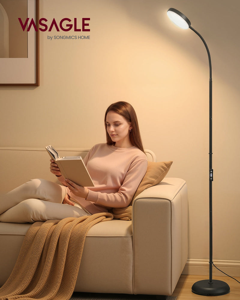 Vasagle floor lamp beside a sofa giving warm reading light while a woman reads a book