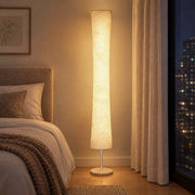 Lit floor lamp beside a bed in the evening