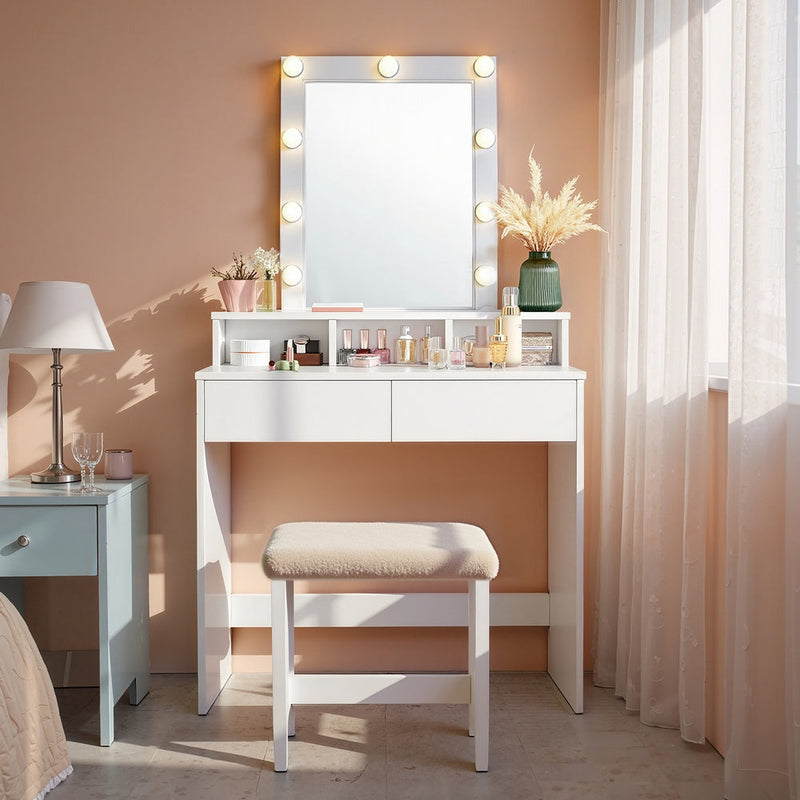White dressing table styled in a bedroom with a matching stool and warm lighting