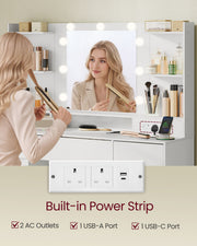 Woman styling her hair at the lit mirror, with a close-up of the power strip showing 2 sockets, USB-A and USB-C