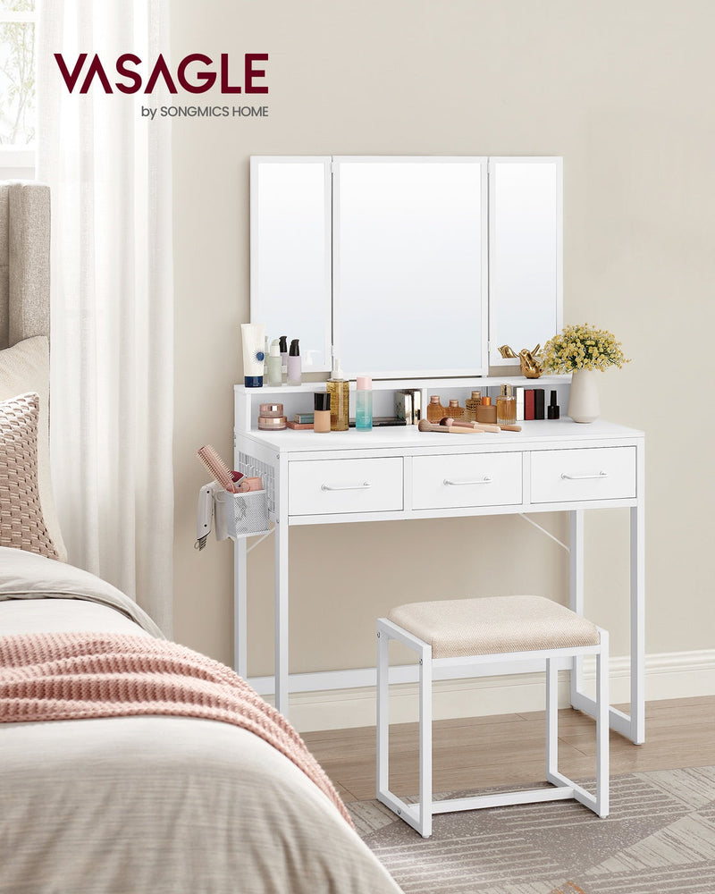 White vanity table with tri-fold mirror and stool styled beside a bed