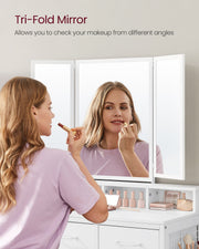 Woman applying lipstick at the white dressing table using the tri-fold mirror