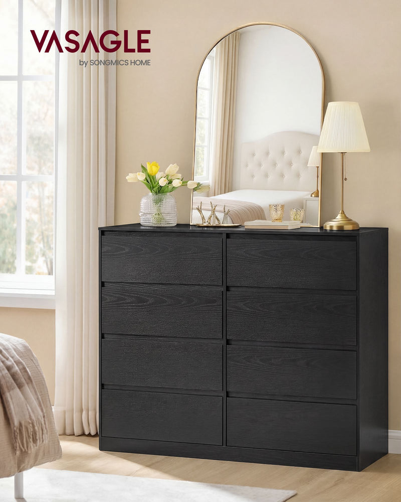 Black 8 drawer chest in a bedroom beneath an arched mirror and table lamp