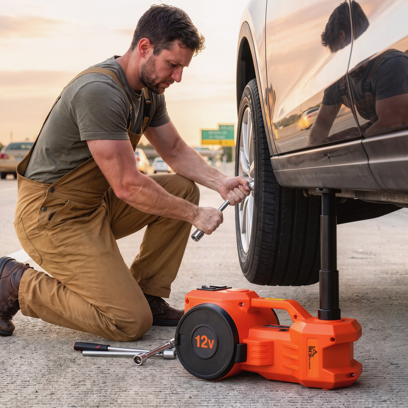 Man changing a wheel on a roadside with the orange electric car jack lifting the car
