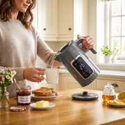 Pouring hot water from the grey electric kettle into a mug at the breakfast table