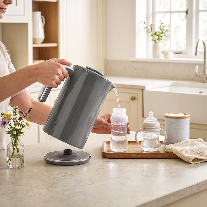 Pouring hot water from the grey electric kettle into a baby bottle