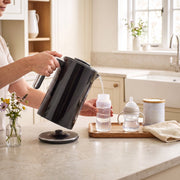 Pouring hot water from the black electric kettle into a baby bottle