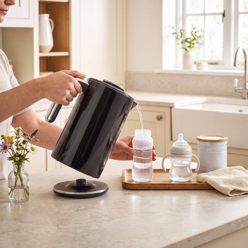 Pouring hot water from the black electric kettle into a baby bottle