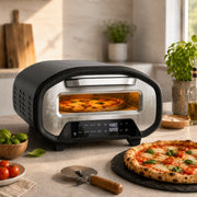 Electric pizza oven on a kitchen worktop baking a margherita pizza, with a finished pizza on a slate board alongside