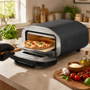 Gloved hand sliding a baked pizza off the ceramic stone of the dial-control oven with a wooden peel