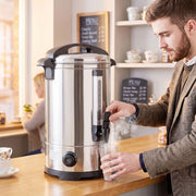 Man drawing hot water from the urn behind a cafe counter with a menu board behind