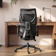 Black mesh office chair seen from behind facing a wooden desk with a lamp