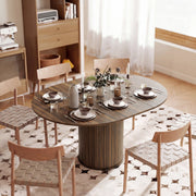 Oval walnut table set for a meal with woven-seat chairs next to a shelving unit