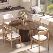 Extended oval walnut table with six cream-cushioned chairs beside a window and a vase of roses