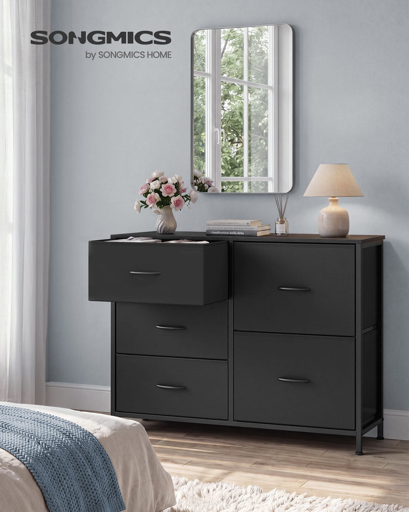 Ink black 5 drawer fabric chest in a bedroom with one drawer open beside a mirror and lamp