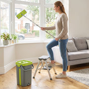 Woman cleaning a high window with the long-handled mop, bucket and step stool on the floor