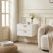 Single white fluted bedside table mounted beside a cream armchair by a window