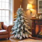 5ft flocked Christmas tree in a cosy living room beside an armchair and fireplace