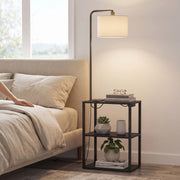Black floor lamp with shelf table at a bedside with a plant and glasses on top